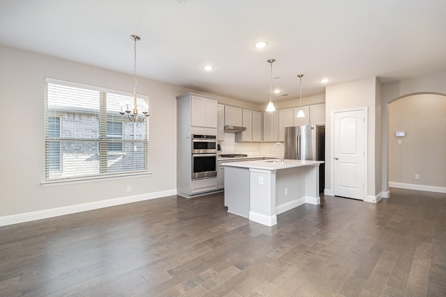 kitchen with sink, an island with sink, appliances with stainless steel finishes, decorative light fixtures, and dark hardwood / wood-style flooring