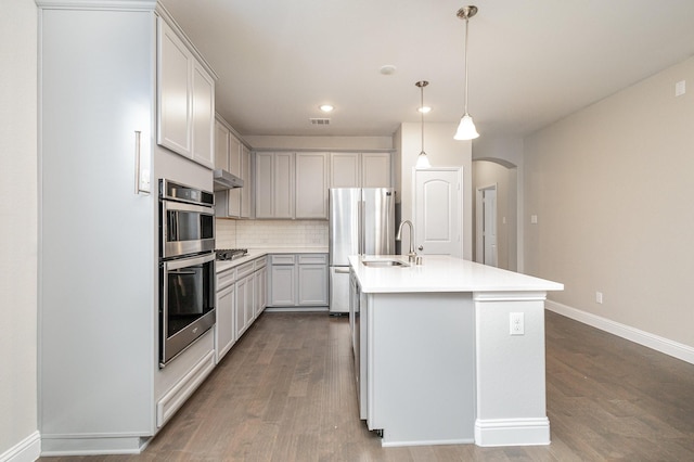 kitchen featuring sink, hardwood / wood-style floors, decorative light fixtures, a center island with sink, and appliances with stainless steel finishes