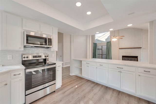 kitchen featuring white cabinets, a large fireplace, light wood-type flooring, and appliances with stainless steel finishes