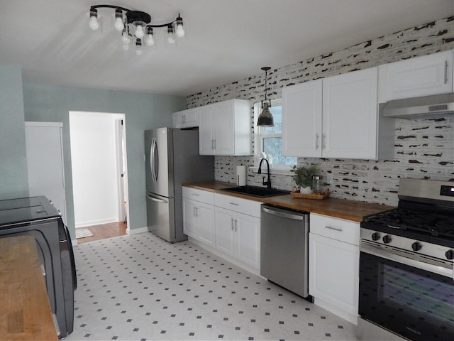 kitchen with butcher block counters, white cabinetry, sink, exhaust hood, and appliances with stainless steel finishes