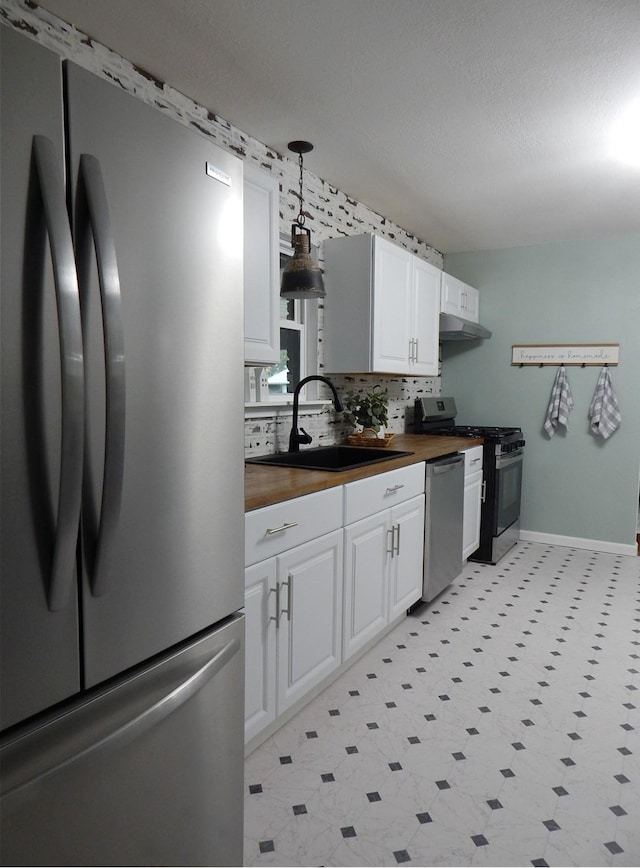 kitchen featuring wood counters, sink, appliances with stainless steel finishes, decorative light fixtures, and white cabinetry