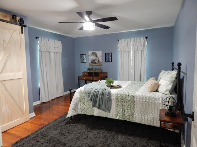 bedroom featuring a barn door, ceiling fan, and dark hardwood / wood-style floors