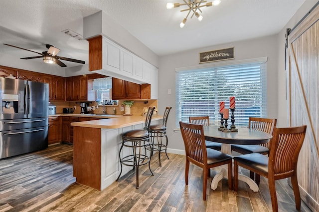 kitchen with dark hardwood / wood-style flooring, a barn door, kitchen peninsula, and stainless steel refrigerator with ice dispenser