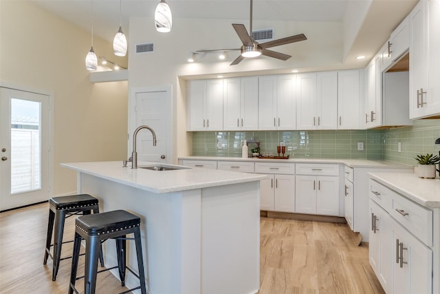 kitchen with a kitchen island with sink, ceiling fan, sink, light hardwood / wood-style flooring, and white cabinets