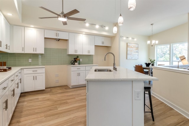 kitchen with a center island with sink, white cabinets, sink, decorative backsplash, and light hardwood / wood-style floors