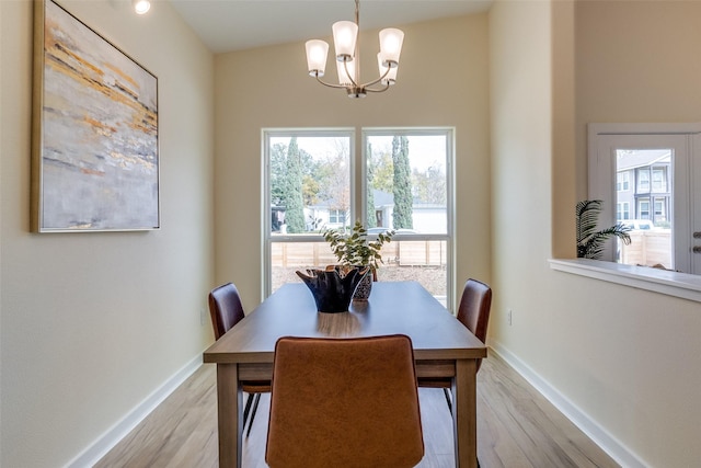 dining space with light wood-type flooring, vaulted ceiling, and an inviting chandelier