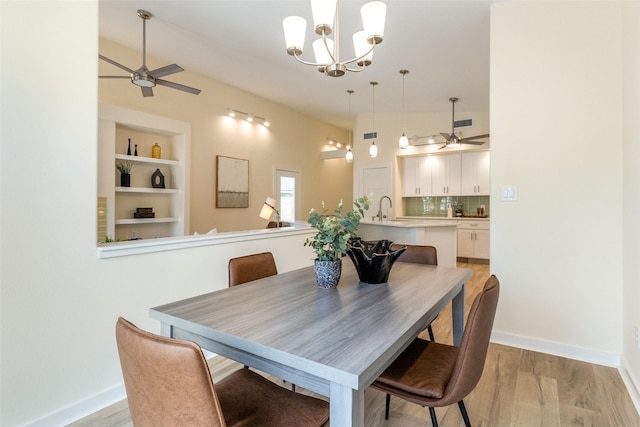 dining room with light wood-type flooring, built in shelves, and ceiling fan with notable chandelier