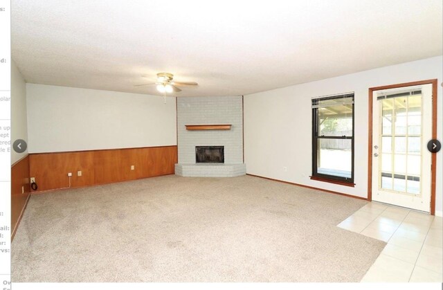 unfurnished living room with ceiling fan, light colored carpet, a fireplace, and wooden walls