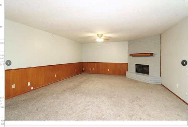 unfurnished living room with light carpet, wooden walls, ceiling fan, and a brick fireplace