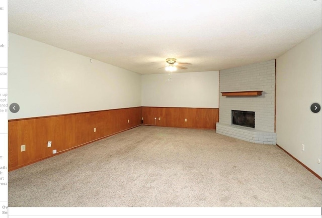 unfurnished living room featuring wooden walls, a fireplace, light colored carpet, ceiling fan, and a textured ceiling