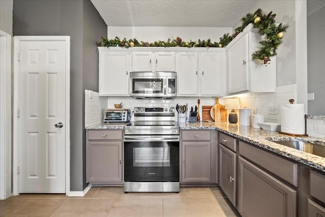 kitchen featuring stainless steel appliances, white cabinetry, gray cabinets, and decorative backsplash