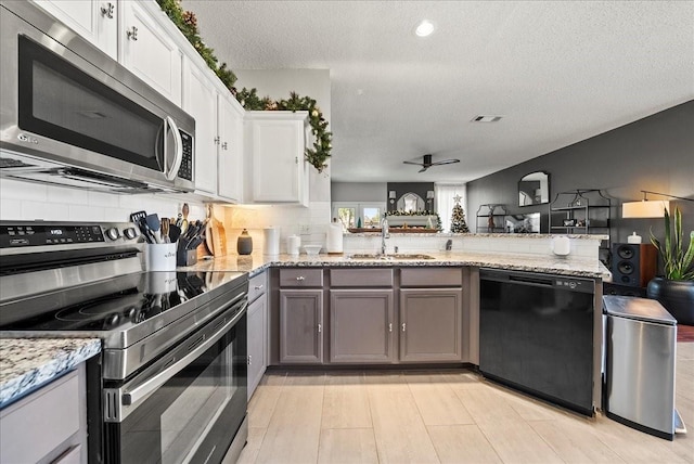 kitchen featuring white cabinetry, sink, kitchen peninsula, stainless steel appliances, and light stone countertops