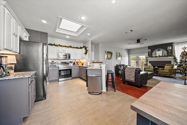 kitchen with gray cabinets, a skylight, sink, a kitchen breakfast bar, and stainless steel appliances