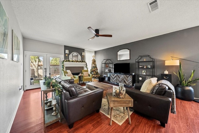 living room with a textured ceiling, dark wood-type flooring, french doors, and ceiling fan