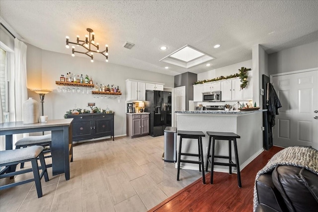 kitchen with white cabinetry, light stone counters, a kitchen bar, black refrigerator with ice dispenser, and kitchen peninsula