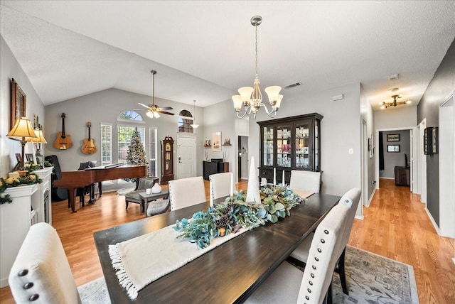 dining space featuring ceiling fan with notable chandelier, light hardwood / wood-style flooring, a textured ceiling, and vaulted ceiling