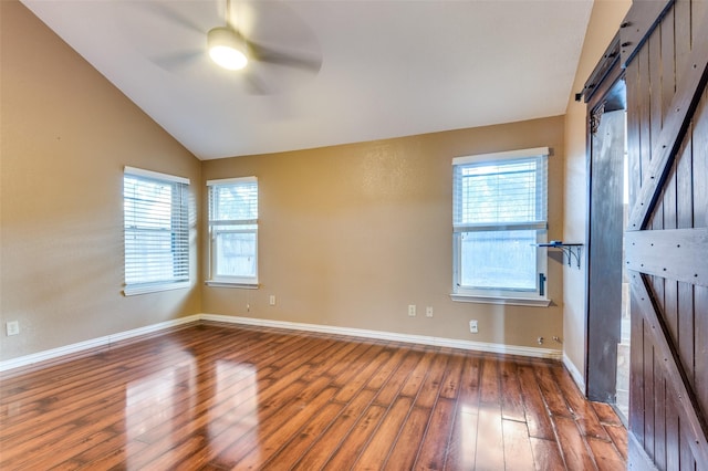 unfurnished room with a barn door, dark hardwood / wood-style floors, vaulted ceiling, and ceiling fan