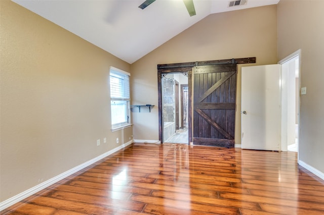 empty room with a barn door, ceiling fan, hardwood / wood-style floors, and lofted ceiling