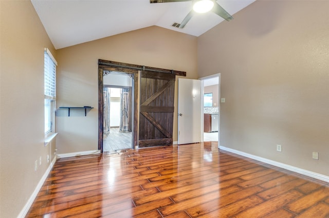 spare room featuring ceiling fan, a barn door, wood-type flooring, and vaulted ceiling