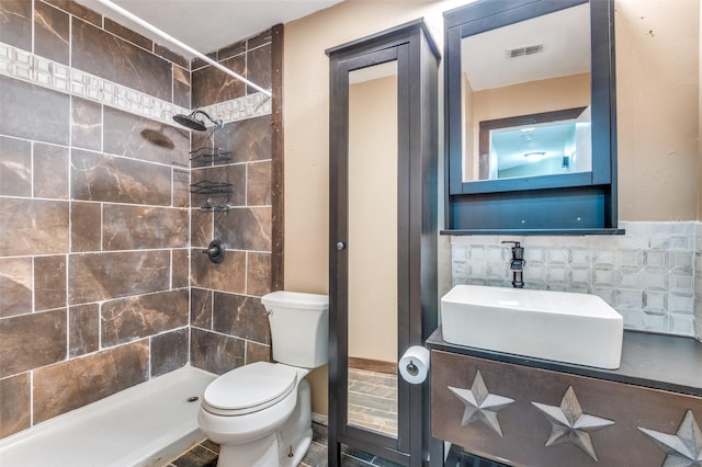 bathroom featuring vanity, toilet, tiled shower, and tile walls