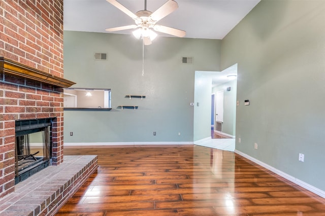 unfurnished living room with a high ceiling, hardwood / wood-style flooring, a brick fireplace, and ceiling fan