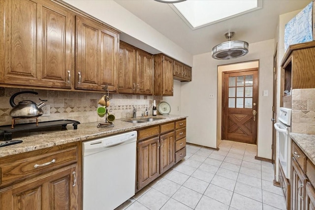 kitchen with tasteful backsplash, light stone counters, white appliances, sink, and light tile patterned floors