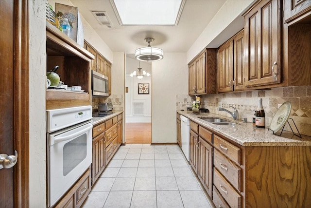 kitchen featuring light stone countertops, white appliances, sink, an inviting chandelier, and light tile patterned flooring