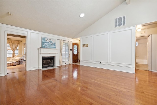 unfurnished living room with high vaulted ceiling, a healthy amount of sunlight, a textured ceiling, and light wood-type flooring