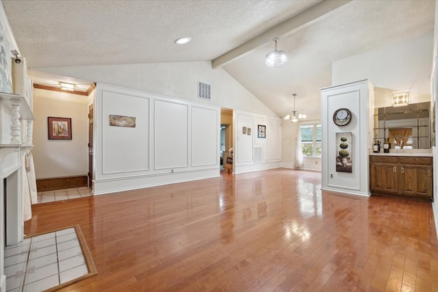 unfurnished living room featuring vaulted ceiling with beams, light hardwood / wood-style floors, a textured ceiling, and an inviting chandelier