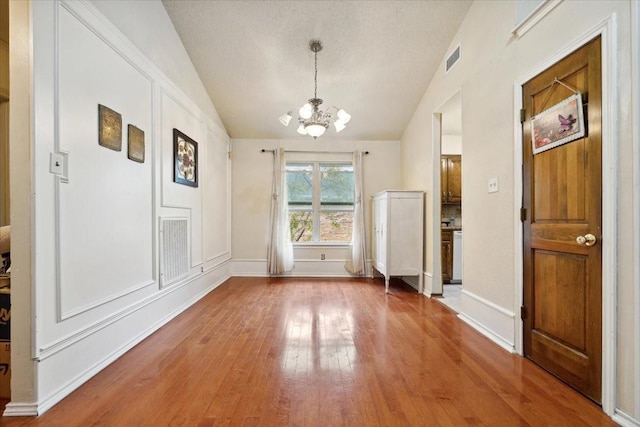 unfurnished dining area featuring a textured ceiling, wood-type flooring, vaulted ceiling, and a notable chandelier