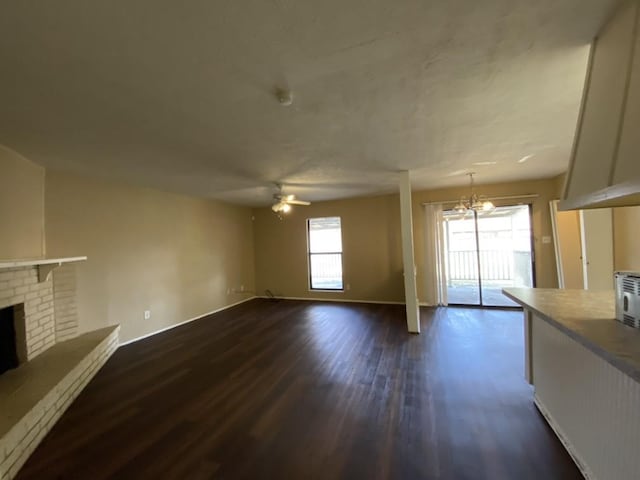 unfurnished living room with dark hardwood / wood-style flooring, ceiling fan with notable chandelier, and a brick fireplace