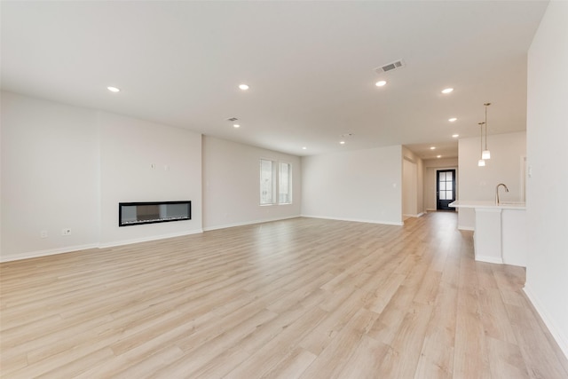 unfurnished living room featuring sink and light hardwood / wood-style flooring