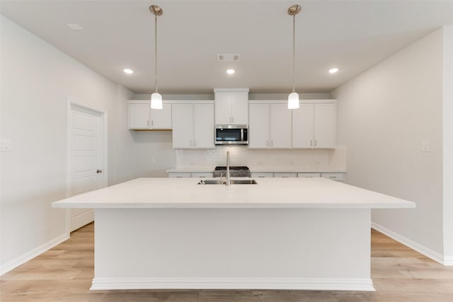 kitchen featuring an island with sink, sink, and white cabinets