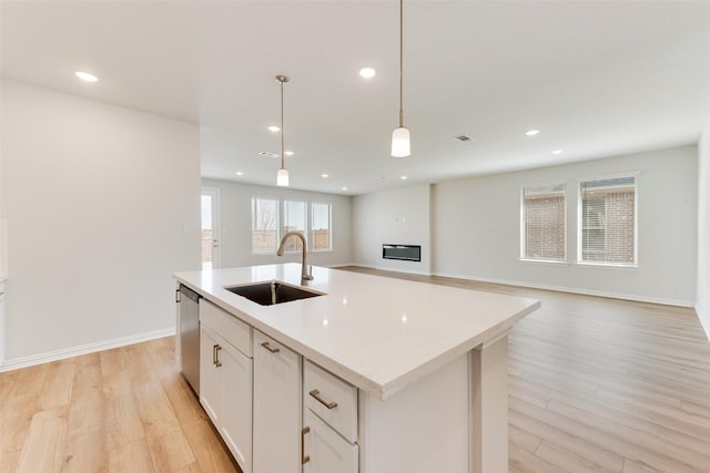 kitchen with sink, decorative light fixtures, light hardwood / wood-style flooring, dishwasher, and an island with sink