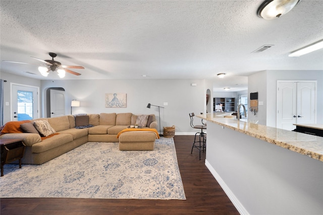 living room with a textured ceiling, ceiling fan, dark wood-type flooring, and sink