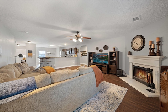 living room featuring a textured ceiling, ceiling fan, and dark wood-type flooring