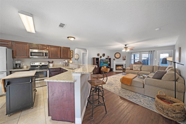 kitchen with kitchen peninsula, appliances with stainless steel finishes, a kitchen bar, sink, and light hardwood / wood-style flooring