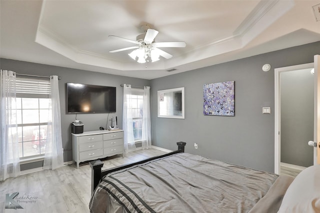 bedroom with multiple windows, a tray ceiling, light hardwood / wood-style flooring, and ornamental molding