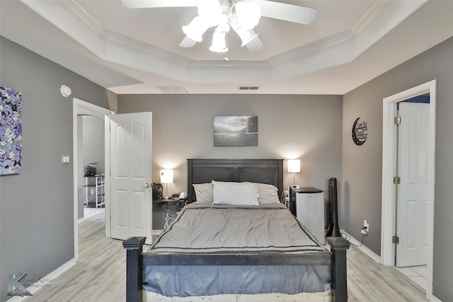 bedroom featuring ceiling fan, ornamental molding, a tray ceiling, and light hardwood / wood-style flooring