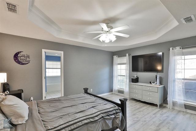 bedroom with crown molding, light hardwood / wood-style flooring, ceiling fan, and a tray ceiling