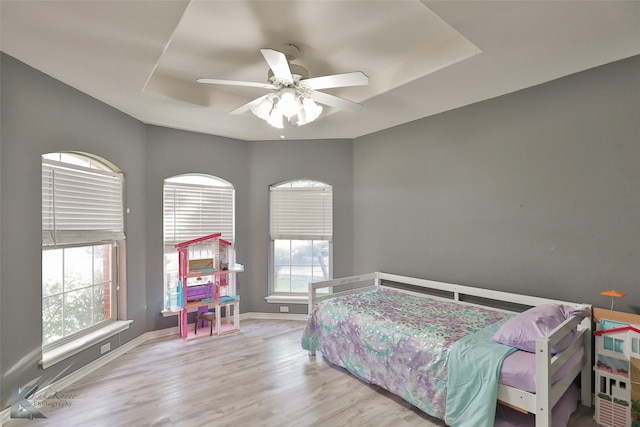 bedroom with a tray ceiling, ceiling fan, and light wood-type flooring