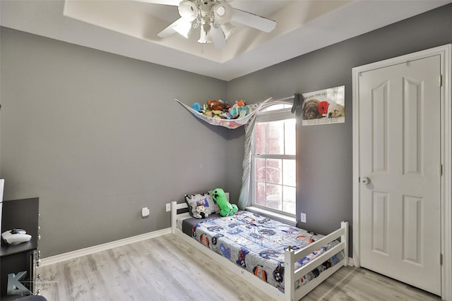 bedroom featuring ceiling fan, light wood-type flooring, and a tray ceiling