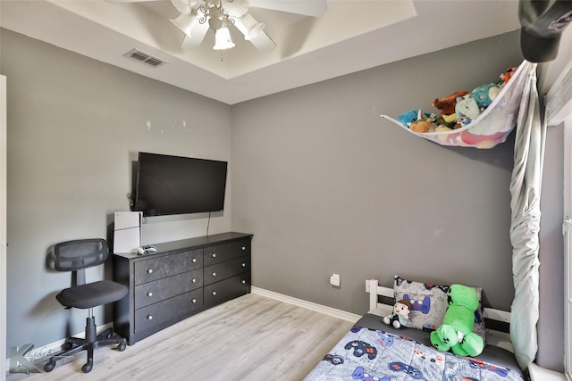 bedroom with a tray ceiling, ceiling fan, and light wood-type flooring