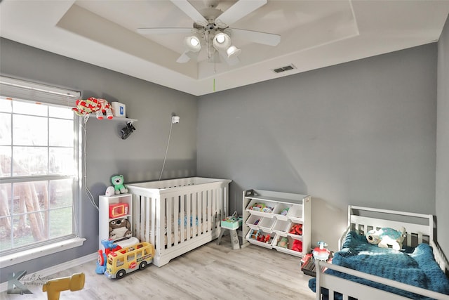 bedroom featuring a raised ceiling, hardwood / wood-style flooring, and multiple windows