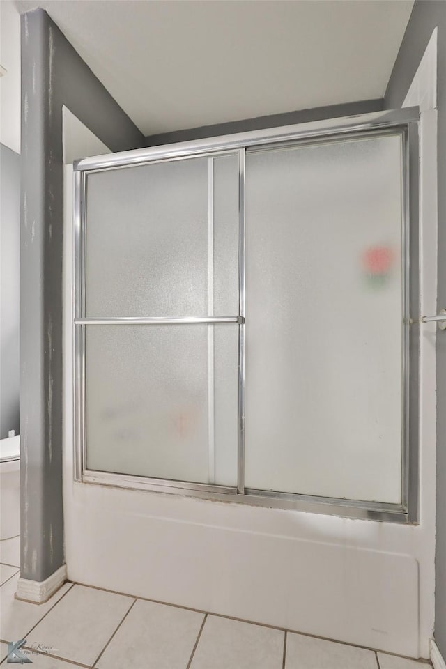 bathroom with tile patterned flooring, combined bath / shower with glass door, and toilet