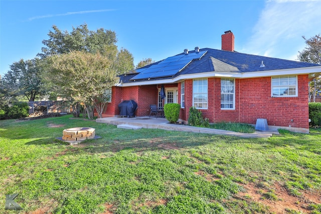 back of property featuring a patio area, a lawn, solar panels, and an outdoor fire pit