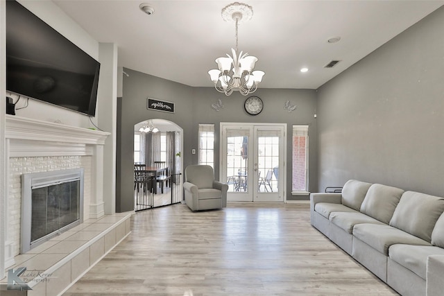 living room with a notable chandelier, light hardwood / wood-style flooring, a fireplace, and french doors