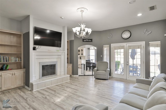 living room with an inviting chandelier, light hardwood / wood-style floors, a tile fireplace, and french doors