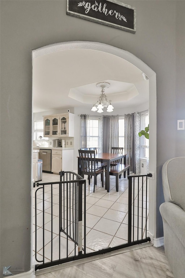 dining space featuring light tile patterned flooring, a tray ceiling, and a notable chandelier