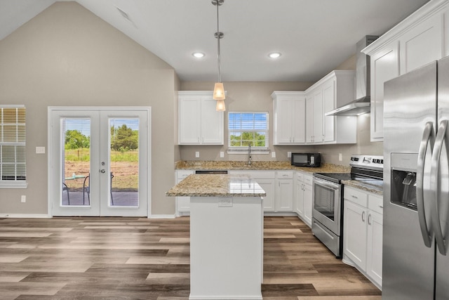 kitchen with appliances with stainless steel finishes, white cabinetry, hanging light fixtures, a kitchen island, and wall chimney exhaust hood